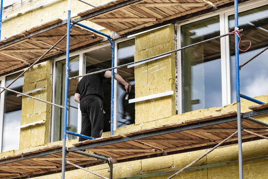 Workers are applying mineral wool insulation to the exterior walls of a commercial building under renovation. Scaffolding supports their work