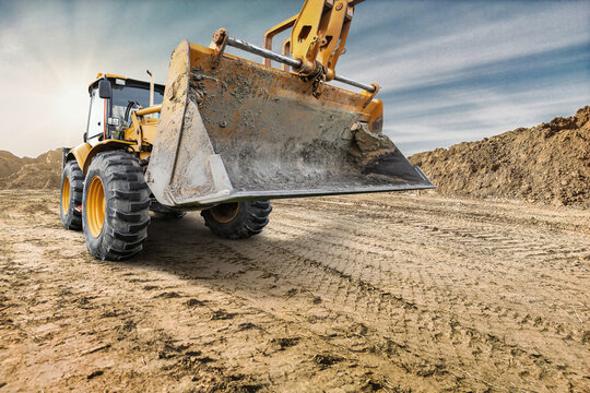 Heavy equipment is operating on a construction site to move dirt and materials during the day. The sun is shining on the work area