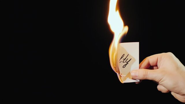 A man's hand holds a burning paper with word loyalty against black background symbolizing betrayal.