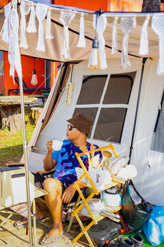 Young Asian man sitting outside a canvas tent enjoying coffee during a glamping trip