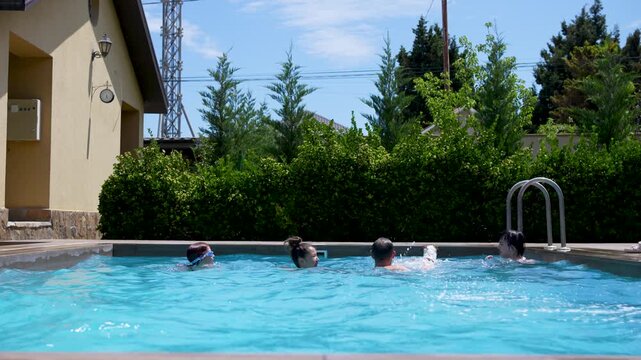 Happy family swimming, splashing water, and having fun in an outdoor pool while a Jack Russell terrier dog runs along the poolside on a sunny day
