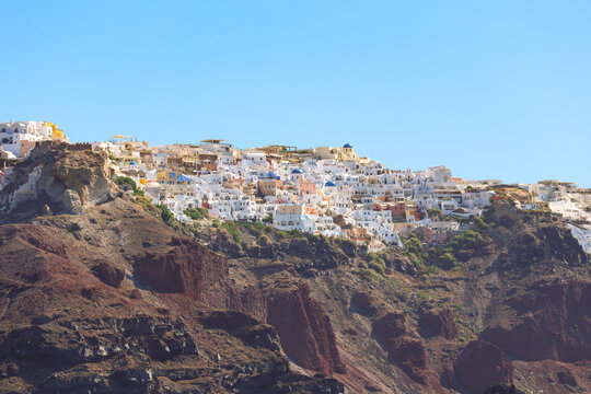 The whitewashed village of Oia perches on volcanic cliffs above the Aegean Sea in Santorini, Greece, glowing under the bright Mediterranean sun.