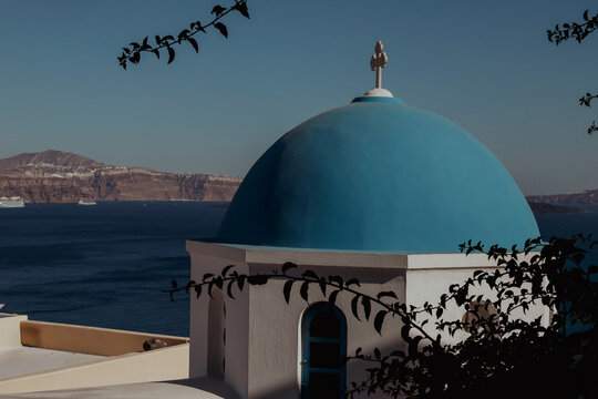 A white church with a blue dome overlooks the Aegean Sea and volcanic cliffs in Santorini, Greece, symbolizing the island&rsquo;s timeless Mediterranean beauty.