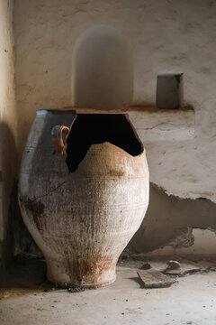 A broken clay vessel stands in a rustic interior in Greece, revealing the texture and patina of traditional craftsmanship.