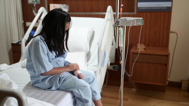 Female patient sits on a hospital bed beside an IV infusion pump while receiving medical care. Concept of hospitalization, healthcare, patient recovery, treatment, and clinical care.