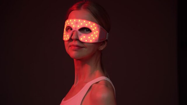 woman wearing an infrared eye mask looks to the side, then turns to the camera and smiles. skincare routine video footage. black background