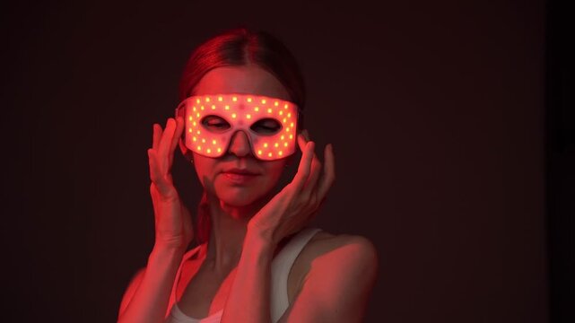 Woman using infrared eye mask. dark background. looking at the camera and smiling. video footage