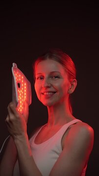 beautiful woman using infrared light face mask. infrared light mask.  black background. professional skin care. vertical video footage.