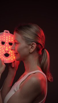 professional skin care. infrared light mask. woman using infrared light face mask. black background. vertical video footage