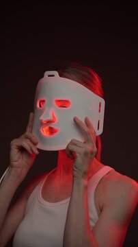 Red light mask. professional skin care. woman using infrared light face mask. black background. vertical video footage
