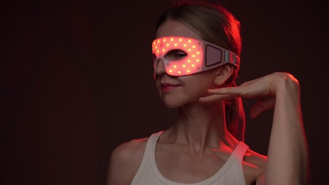 Red and infrared light therapy eye mask. smiling woman wearing infrared light eyes therapy mask. . turns in profile, touches his face with her hand. video footage