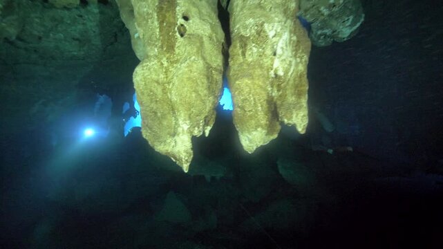 Pendant rock formations fill the foreground while a concentrated blue light glows through the dark water of Cenote Carwash, Quintana Roo, Mexico.