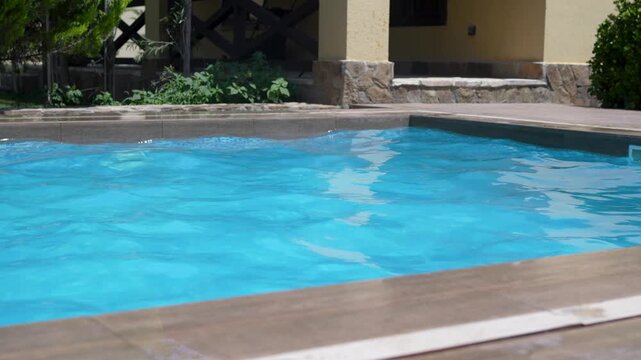Clear blue water softly rippling in an outdoor swimming pool on a sunny summer day in the backyard of a house