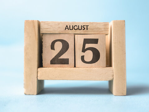 A wooden block calendar for August 25th on a light blue background.