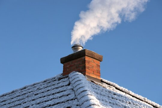 Chimney smoking on snowy roof in winter