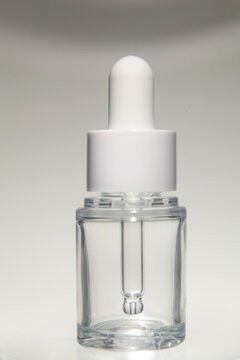 Minimalist clear glass dropper bottle with a white cap isolated on a neutral background. Blank cosmetic packaging mockup suitable for skincare, facial serum, essential oil, beauty branding, product pr