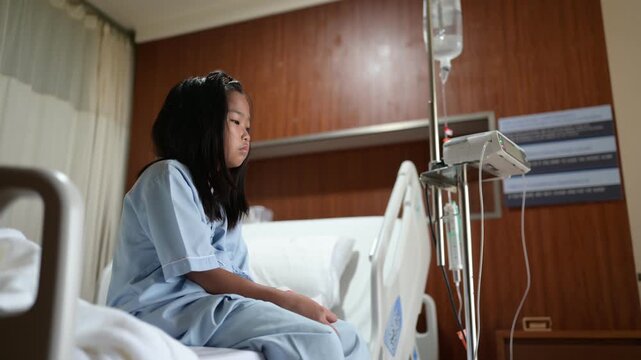 Female patient sits on a hospital bed beside an IV infusion pump while receiving medical care. Concept of hospitalization, healthcare, patient recovery, treatment, and clinical care.