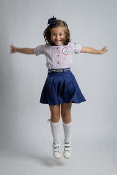 Happy Little Girl in School Uniform Jumping for Joy. Studio Portrait of Excited Student Back to School Concept.