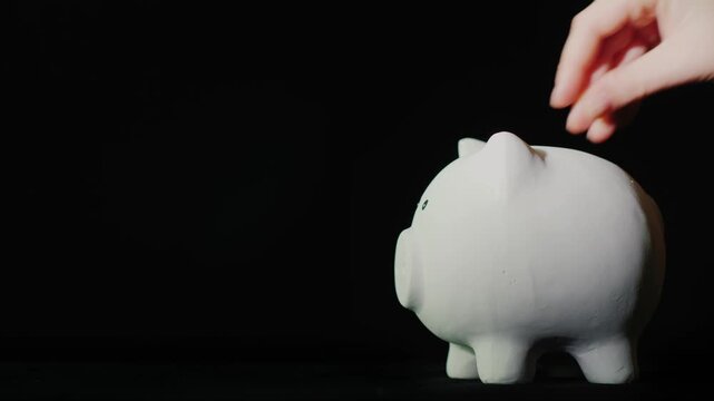 A hand depositing golden bitcoin coin into white piggy bank on black background financial investment and cryptocurrency savings concept.