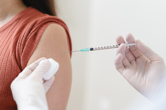 Close up of doctor in blue gloves giving vaccine injection to a female patient.