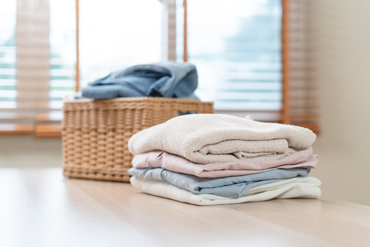 A neat stack of clean folded clothes on wooden table with wicker laundry basket.