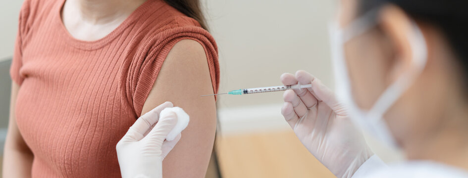 Close up of doctor in blue gloves giving vaccine injection to a female patient.