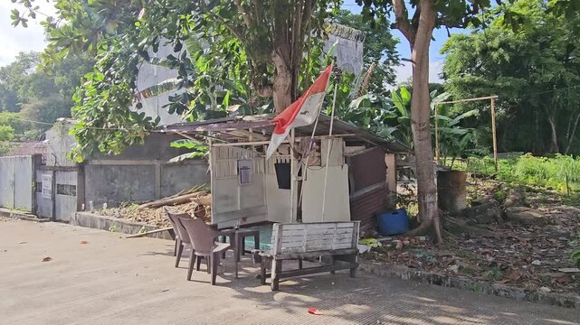 old wooden house,Simple roadside stall under leafy tree shade.. Indonesian flag waves gently in morning breeze. Red white flag or Bendera Merah Putih on Independence day                               