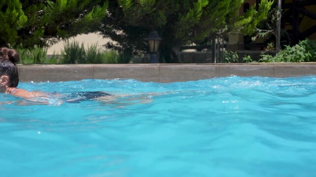 Happy young woman enjoying a refreshing swim in a clear blue outdoor pool at a private villa during summer vacation