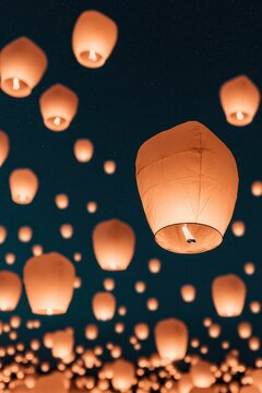 Many sky lanterns float in the night sky during a festival celebration with people watching and enjoying