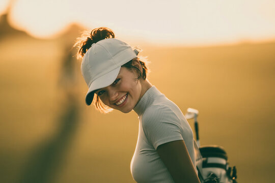 Smiling golfer walks on the course during golden hour with golf clubs in hand