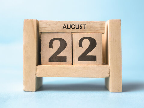 A wooden block calendar for August 22nd on a light blue background.