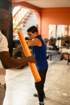 Young man learning boxing with trainer in gymnasium