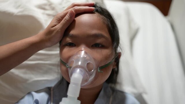 Close-up of a sick child receiving oxygen therapy while resting in a hospital bed as a caregiver checks for fever. Pediatric healthcare, illness, medical treatment, care, and recovery.
