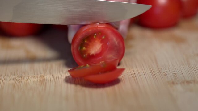 A hand holds a red tomato on a cutting board and slices it with a knife, fresh vegetables. Contains vitamin C and potassium. Healthy eating, nutrition, vegetables, healthy lifestyle, fresh, raw foods.