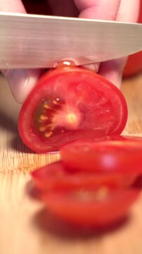 A hand holds a red tomato on a cutting board and slices it with a knife, fresh vegetables. Contains vitamin C and potassium. Healthy eating, nutrition, vegetables, healthy lifestyle, fresh, raw foods.