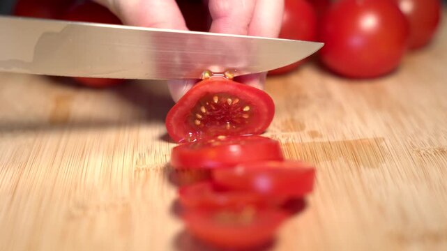 A hand holds a red tomato on a cutting board and slices it with a knife, fresh vegetables. Contains vitamin C and potassium. Healthy eating, nutrition, vegetables, healthy lifestyle, fresh, raw foods.
