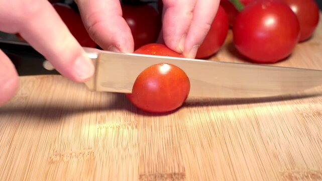 A hand holds a red tomato on a cutting board and slices it with a knife, fresh vegetables. Contains vitamin C and potassium. Healthy eating, nutrition, vegetables, healthy lifestyle, fresh, raw foods.