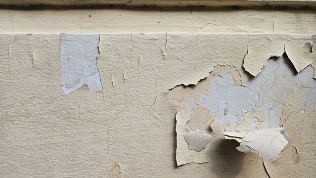 The walls whose paint is peeling off because they are old and exposed to heat and rain, the wall paint is beige. Abstract background texture from a wall with damaged paint.
