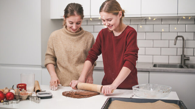 Sisters Roll Gingerbread Dough With A Pin To Even Thickness, Baking Cookies For Christmas Celebration