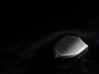 Naklejka premium Minimalist Brushed Steel Shield Emblem Resting on Dark Textured Velvet Fabric for Concepts of Protection and Strength