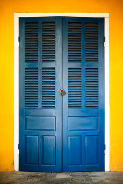 Closed vintage blue wooden louvered doors on yellow facade of ancient building in Hoi An Vietnam, Vietnamese traditional style exterior entrance with doors closed on metal lock against yellow wall.