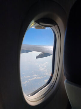 View from an Airplane Window with Wing and Clouds. Passenger Window View of Aircraft Wing in the Sky. Scenic Flight View with Airplane Wing and Clouds.
