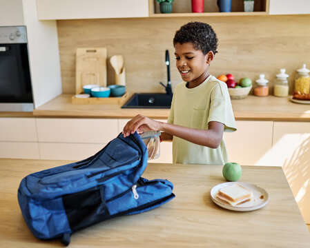 Portret of  a black teen boy with a school backpack having fun alone preparing sanwiches snack for  breakfast and school  in kitchen