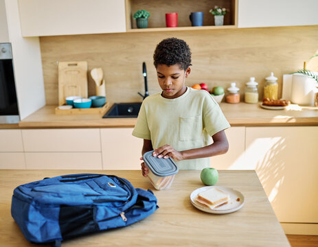 Portret of  a black teen boy with a school backpack having fun alone preparing sanwiches snack for  breakfast and school  in kitchen