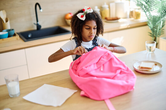 Portret of  a black girl with a school backpack having fun talone preparing sanwiches snack for  breakfast and school  in kitchen