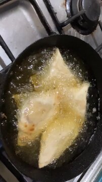 Close up of crispy golden samosas deep frying in hot boiling oil in a pan