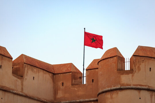 Moroccan flag atop a fortress wall against a clear sky.