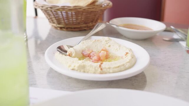 Plate of hummus with olive oil and tomato is served with pita bread and a refreshing drink