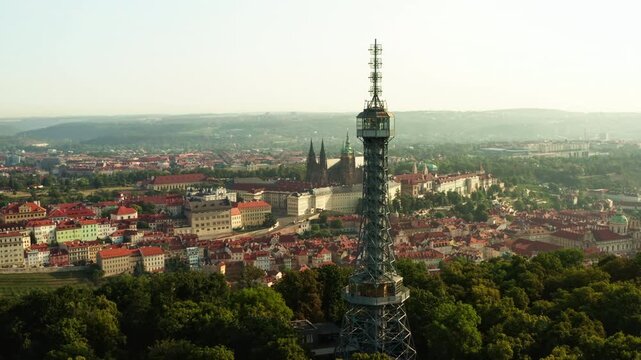Petrin lookout tower rises above green hill park in Prague. Historic Prague Castle and cityscape create famous tourist attraction. Scenic view represents european travel and destination.