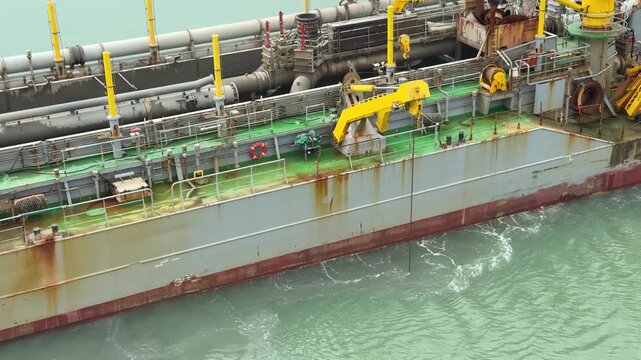 Heavy duty dredge boat clearing sand sediment from ocean floor near harbor quay during maritime engineering works.